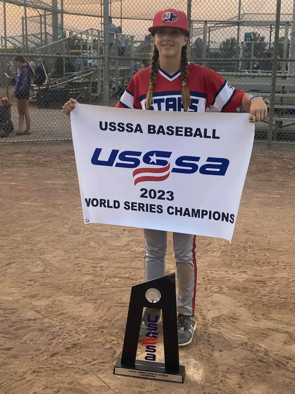 Finleigh Kane holding the USSSA World Series Champions banner with the championship trophy